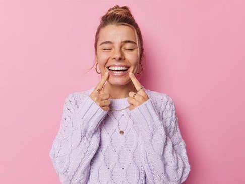 Woman pointing at her teeth after undergoing cosmetic dentistry treatment