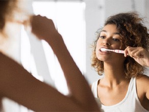 Woman brushing her teeth in the bathroom mirror