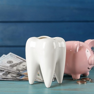 A ceramic model of a tooth, a piggy bank, and some money on a light blue wooden table