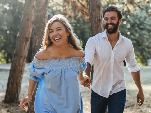 Smiling man and woman holding hands while walking through a forest