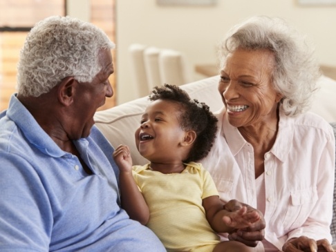 Older man and woman laughing with baby on couch