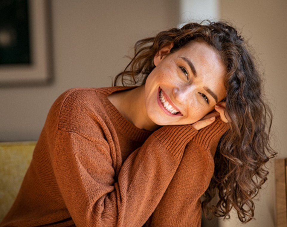 Woman in brown sweater smiling at home